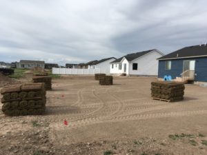 A house with a dirt yard. There are pallets of sod in the yard ready to be laid.