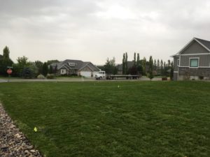 A house with a sod lawn. The sprinklers are on and the flatbed semi truck that carried the sod is on the road in the background.