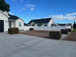 A house with lawn ready for sod. On the sidewalk and driveway are several pallets of sod ready to be installed.